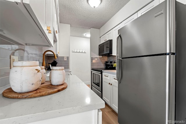 kitchen with stainless steel appliances, light wood-style floors, a textured ceiling, white cabinetry, and backsplash