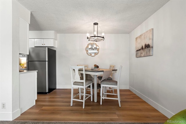 dining space with a notable chandelier, a textured ceiling, baseboards, and wood finished floors