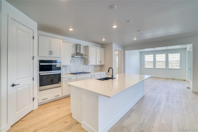 kitchen with stovetop, a sink, decorative backsplash, double oven, and wall chimney range hood