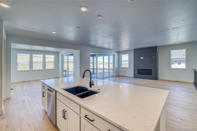 kitchen with a fireplace, a sink, open floor plan, dishwasher, and light wood-type flooring