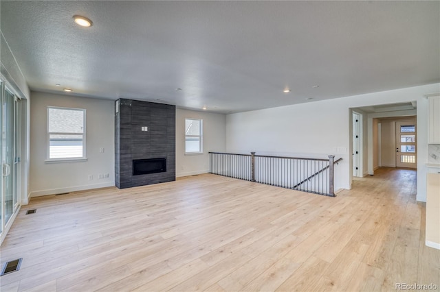 unfurnished living room featuring visible vents, baseboards, a large fireplace, and light wood-style floors