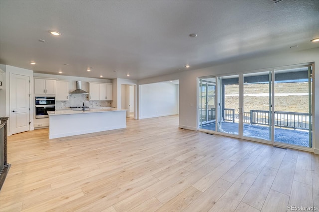 kitchen with tasteful backsplash, open floor plan, white cabinetry, light wood-style floors, and wall chimney exhaust hood