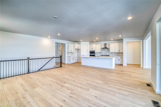 kitchen featuring white cabinetry, wall chimney range hood, open floor plan, and light wood-type flooring