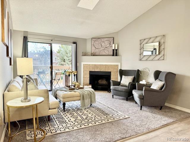 living area with vaulted ceiling with skylight, baseboards, a tiled fireplace, and wood finished floors