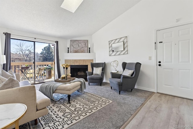 living area featuring baseboards, lofted ceiling with skylight, a tile fireplace, wood finished floors, and a textured ceiling