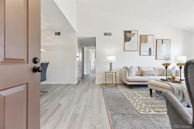 living area featuring visible vents, baseboards, light wood-type flooring, and lofted ceiling