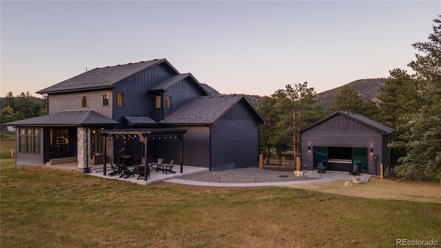 back house at dusk featuring a yard, an outdoor structure, a mountain view, and a patio