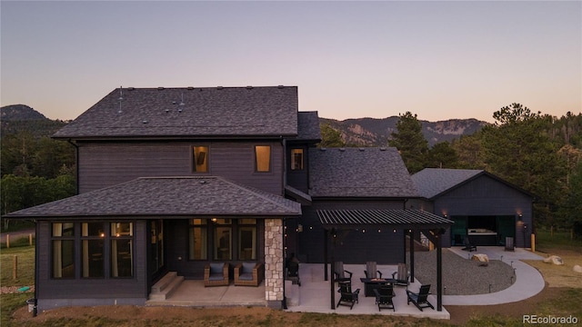 back house at dusk with a yard, a mountain view, and a patio area