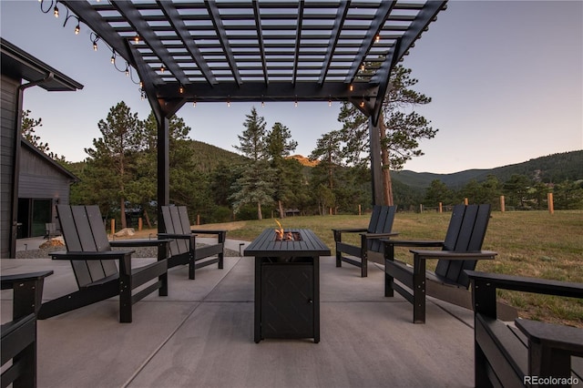 patio terrace at dusk featuring a mountain view, a pergola, a lawn, and an outdoor fire pit