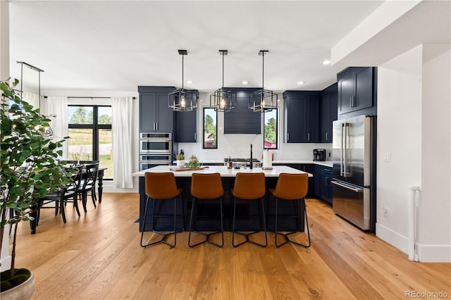 kitchen featuring hanging light fixtures, an island with sink, appliances with stainless steel finishes, and light wood-type flooring