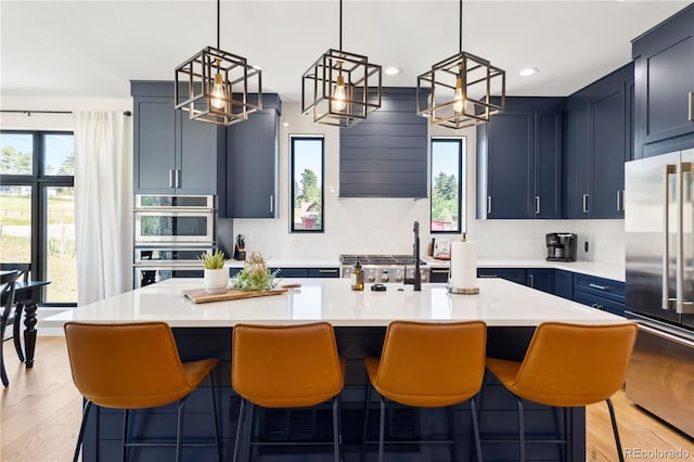 kitchen with stainless steel appliances, an island with sink, blue cabinetry, and a kitchen bar