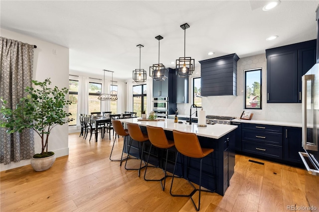 kitchen with a breakfast bar, a center island with sink, decorative light fixtures, wall chimney exhaust hood, and light wood-type flooring