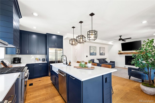 kitchen with blue cabinets, a breakfast bar area, high end appliances, a center island with sink, and pendant lighting