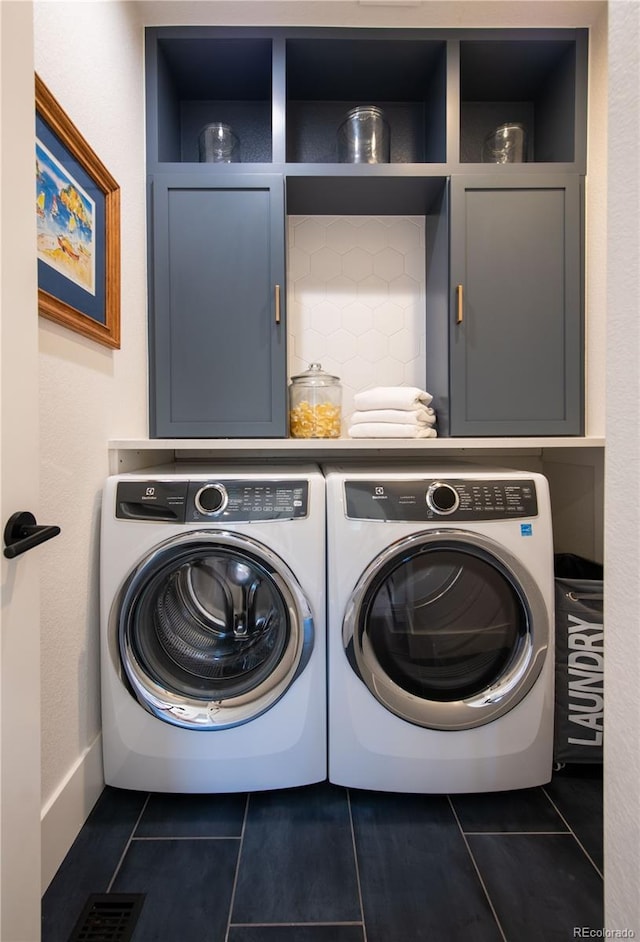 clothes washing area with separate washer and dryer, dark tile patterned flooring, and cabinets