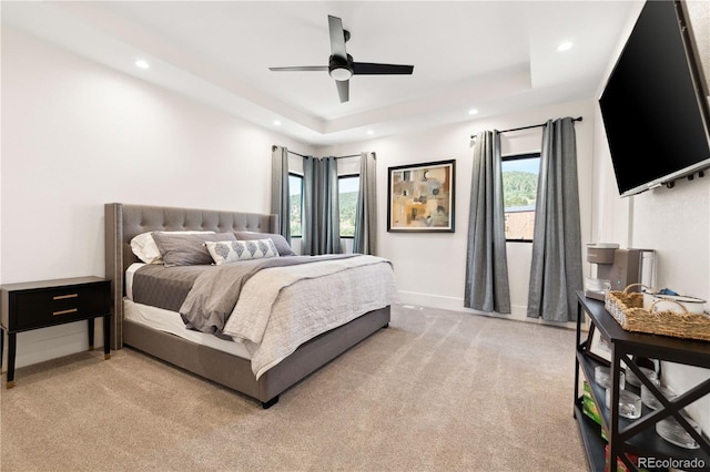 bedroom with multiple windows, light colored carpet, and a tray ceiling