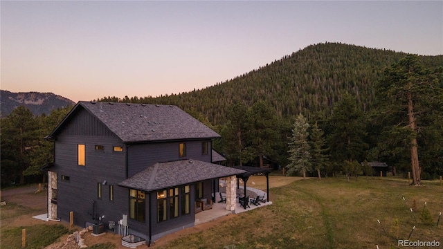 back house at dusk with a patio, a mountain view, and a yard