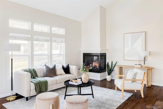 living room with high vaulted ceiling, dark wood-style flooring, baseboards, and a multi sided fireplace