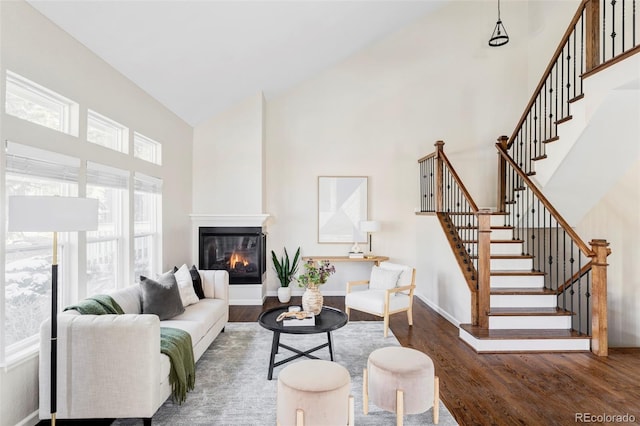 living area featuring high vaulted ceiling, dark wood finished floors, baseboards, stairs, and a glass covered fireplace