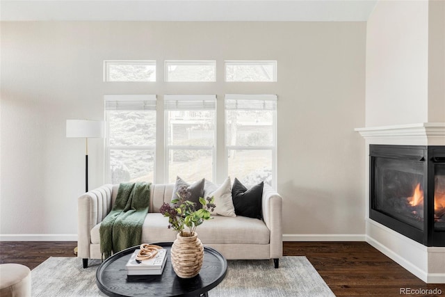 living room featuring dark wood-style floors, a glass covered fireplace, and baseboards