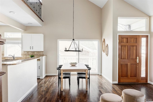 dining space with dark wood-style floors, a towering ceiling, and baseboards