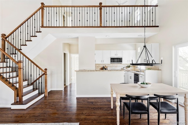 dining room featuring stairway, dark wood-style flooring, a towering ceiling, and baseboards