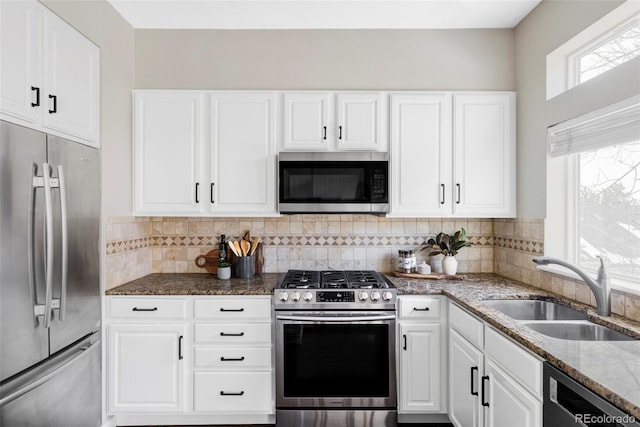 kitchen featuring a sink, white cabinetry, appliances with stainless steel finishes, backsplash, and dark stone counters