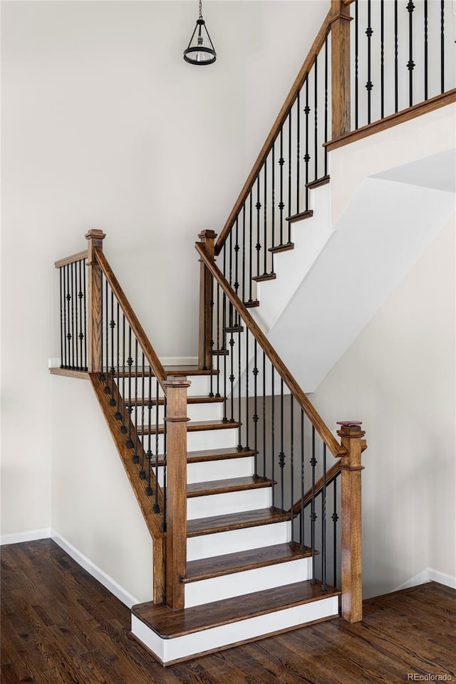 staircase featuring wood finished floors, a towering ceiling, and baseboards