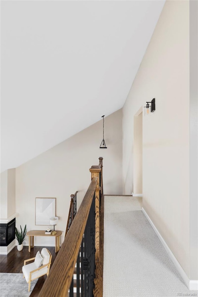 corridor with baseboards, vaulted ceiling, and an upstairs landing