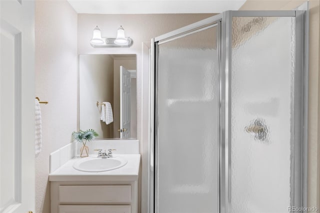 full bath with a textured wall, a shower stall, and vanity