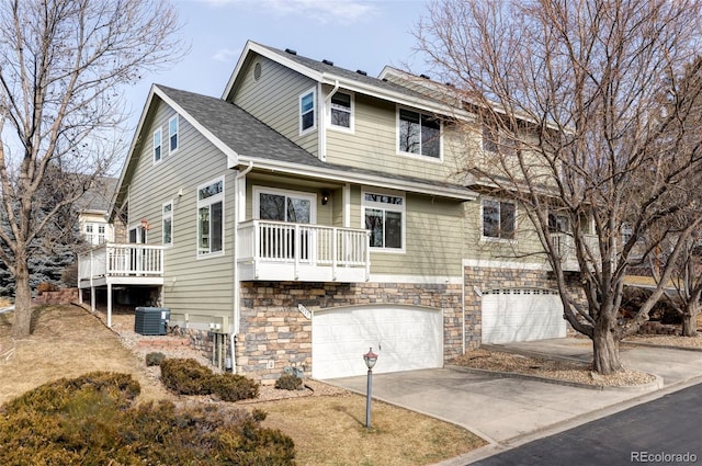 view of front of home with driveway, a shingled roof, stone siding, an attached garage, and cooling unit