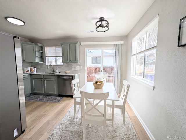 dining area featuring light wood-style flooring, baseboards, visible vents, and a textured wall