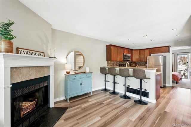 1172 S Zeno Way Unit F, Aurora, CO 80017 - kitchen with stainless steel appliances, light wood-style floors, a peninsula, a tile fireplace, and a kitchen breakfast bar
