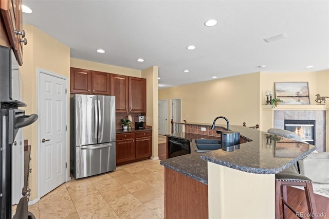 6542 S Tempe St, Aurora, CO 80016 - kitchen with freestanding refrigerator, black dishwasher, a breakfast bar, a large island with sink, and a fireplace