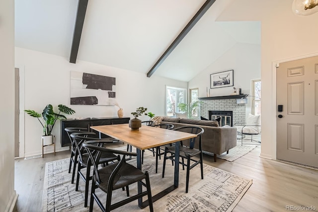 dining space with high vaulted ceiling, light wood-style floors, a brick fireplace, and beam ceiling