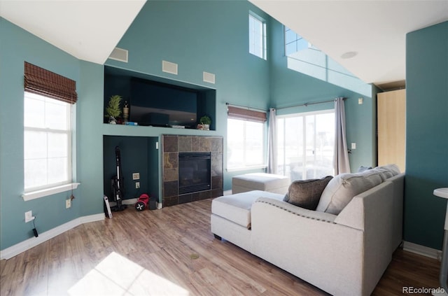 living room featuring a tile fireplace, a towering ceiling, and hardwood / wood-style floors