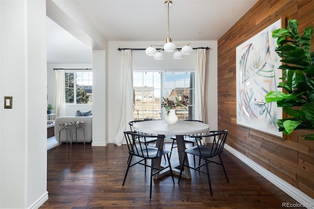 dining area with dark hardwood / wood-style flooring, an inviting chandelier, and wood walls