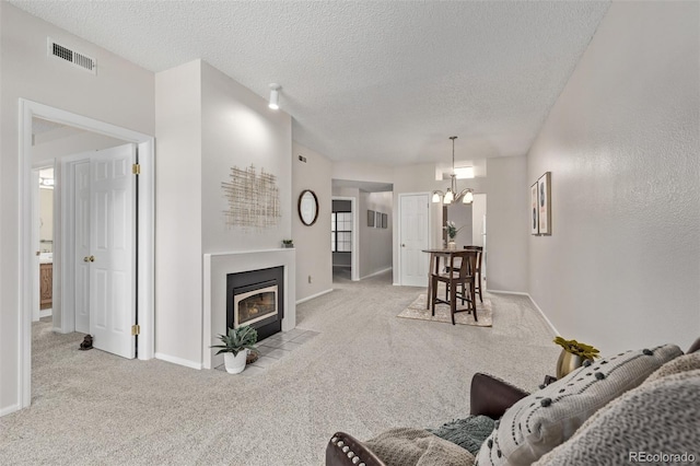 carpeted living area with visible vents, baseboards, a fireplace with flush hearth, a notable chandelier, and a textured ceiling