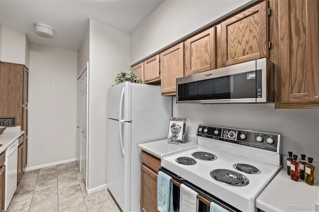 kitchen with brown cabinets, white appliances, light countertops, and baseboards