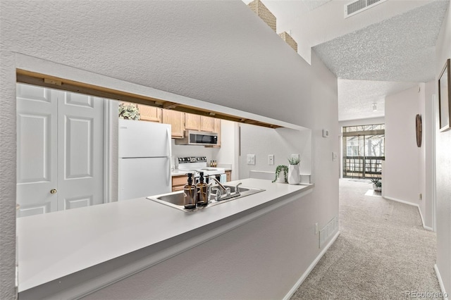 kitchen with white appliances, a peninsula, a sink, a textured ceiling, and light colored carpet