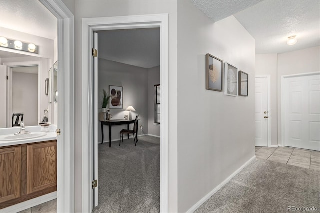 hallway with a sink, baseboards, light carpet, and a textured ceiling