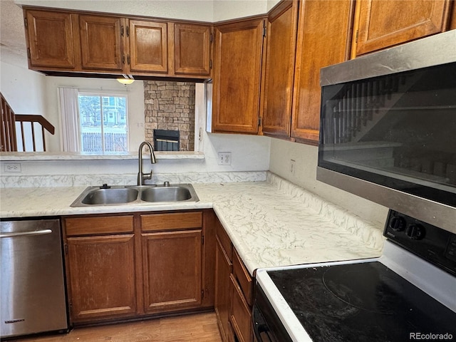 kitchen featuring light wood-type flooring, appliances with stainless steel finishes, a stone fireplace, and sink