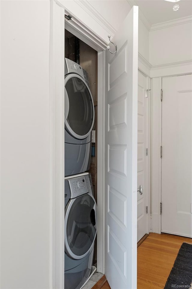 clothes washing area with stacked washing maching and dryer, light wood-type flooring, and ornamental molding