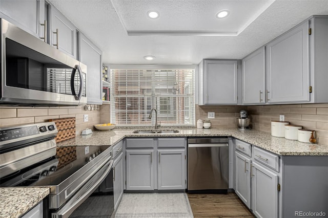 7684 S Monaco Cir, Centennial, CO 80112 - kitchen featuring appliances with stainless steel finishes, gray cabinets, a textured ceiling, decorative backsplash, and wood finished floors