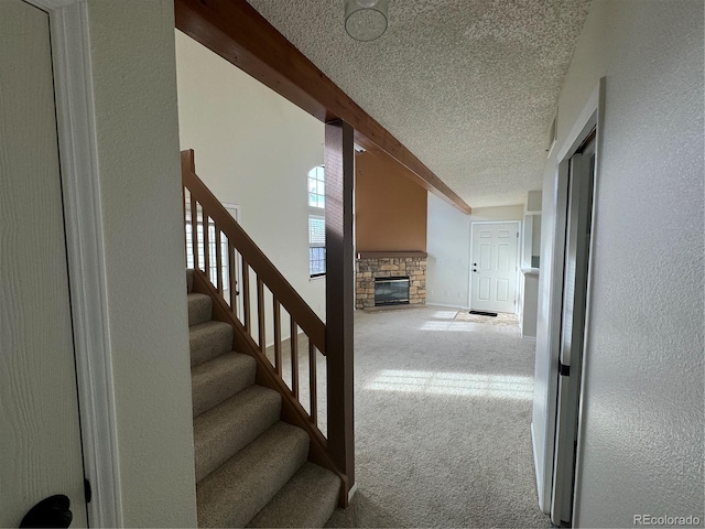 staircase with a stone fireplace, carpet flooring, a textured ceiling, and baseboards