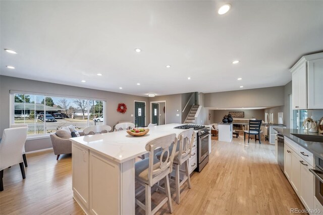 5404 W Rowland Pl, Littleton, CO 80128 - kitchen with stainless steel appliances, a kitchen island, light wood-style flooring, a breakfast bar, and white cabinetry