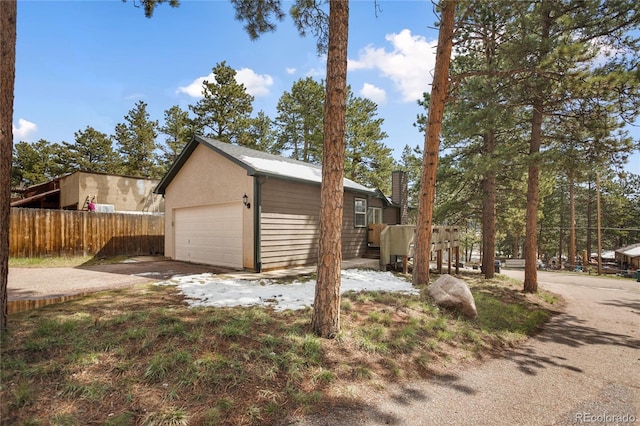 view of home's exterior with fence, concrete driveway, an attached garage, stucco siding, and an outdoor structure