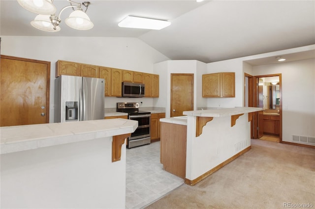 kitchen featuring stainless steel appliances, a breakfast bar, vaulted ceiling, tile countertops, and a peninsula