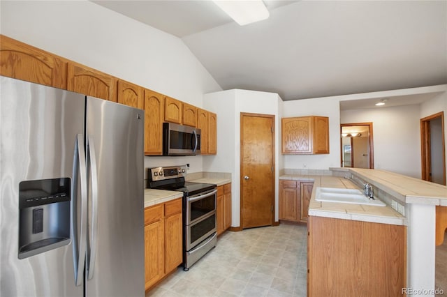 kitchen with appliances with stainless steel finishes, a sink, a peninsula, vaulted ceiling, and brown cabinets