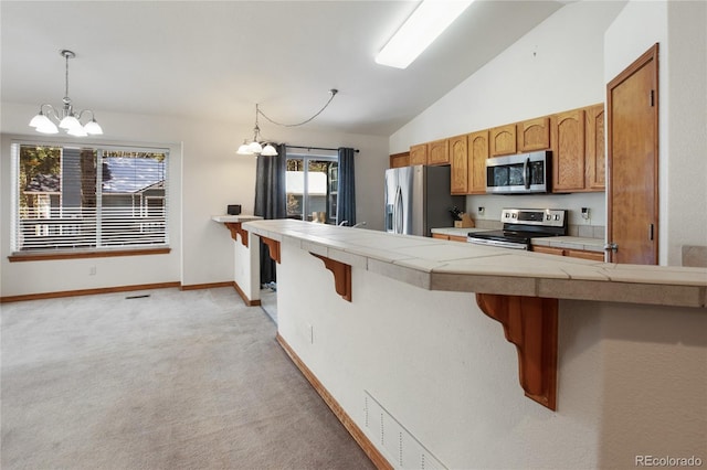 kitchen with appliances with stainless steel finishes, a chandelier, lofted ceiling, light colored carpet, and a kitchen bar