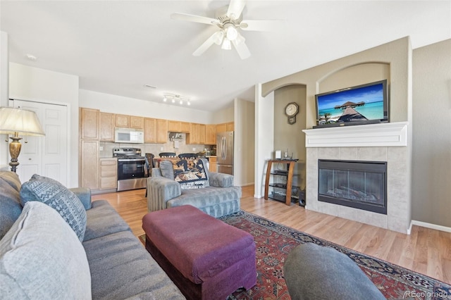 living room with ceiling fan, light hardwood / wood-style flooring, a tiled fireplace, and track lighting